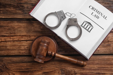 Book with words CRIMINAL LAW, handcuffs and gavel on wooden table, flat lay