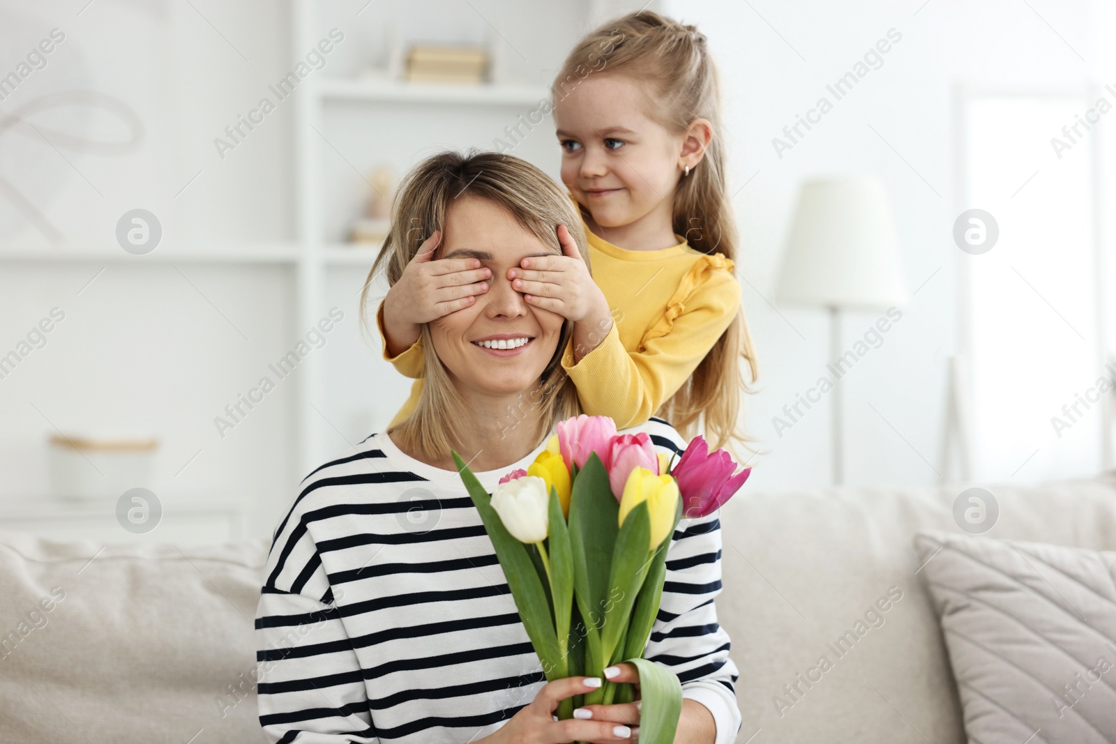 Photo of Little girl surprising her mom with bouquet of tulips at home. Happy Mother`s Day