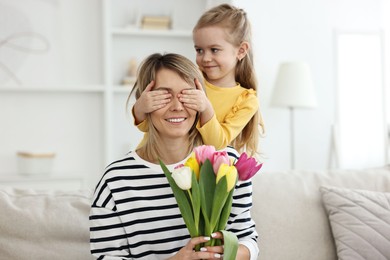 Photo of Little girl surprising her mom with bouquet of tulips at home. Happy Mother`s Day