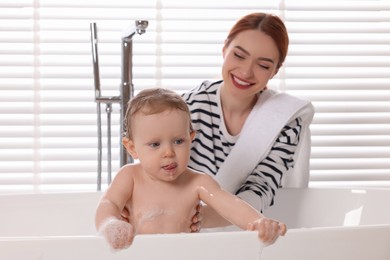Photo of Mother washing her little baby in tub at home, selective focus