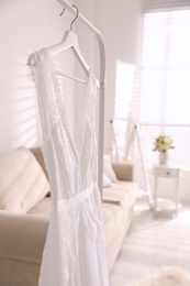Photo of Beautiful wedding dress hanging on rack in room, closeup