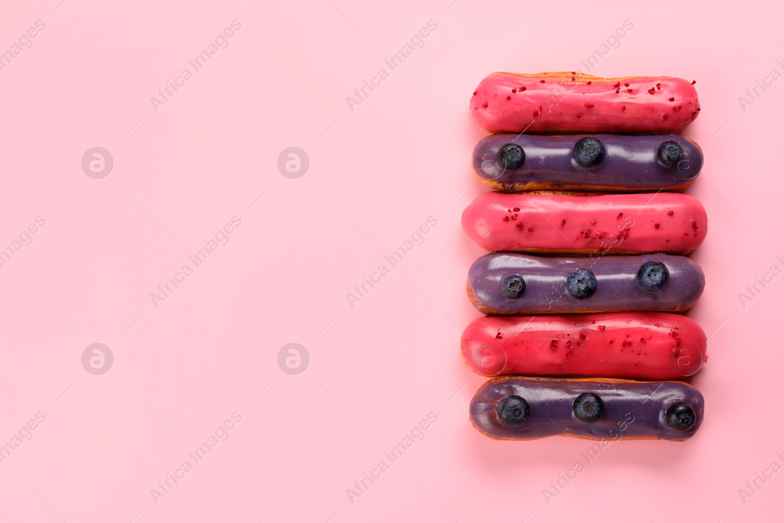 Photo of Delicious eclairs covered with glaze on pink background, top view. Space for text