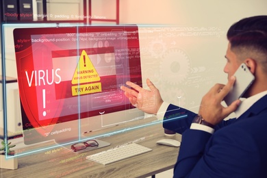 Image of Office worker in front of computer with warning about virus attack on screen