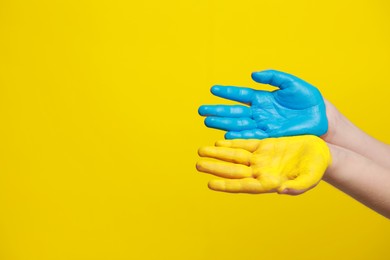 Photo of Little boy with hands painted in Ukrainian flag colors on yellow background, closeup and space for text. Love Ukraine concept