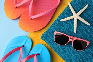 Flip flops, towels, starfish and sunglasses on light blue background, flat lay. Beach accessories