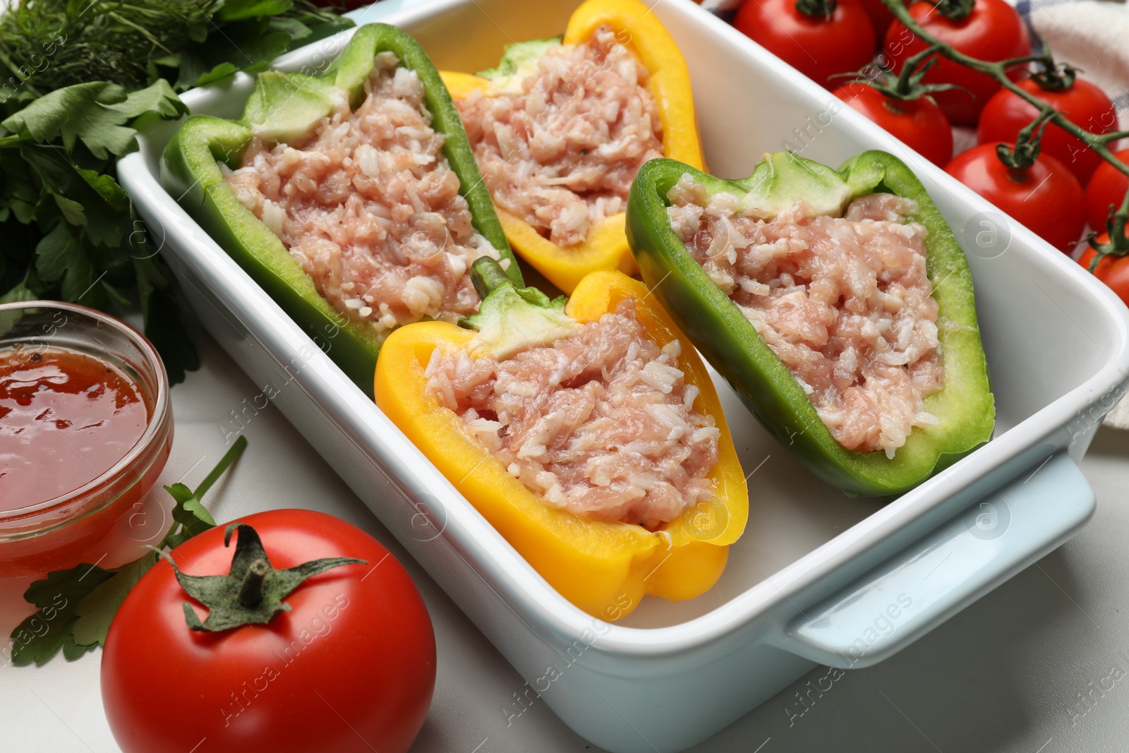 Photo of Raw stuffed peppers and ingredients on white table, closeup