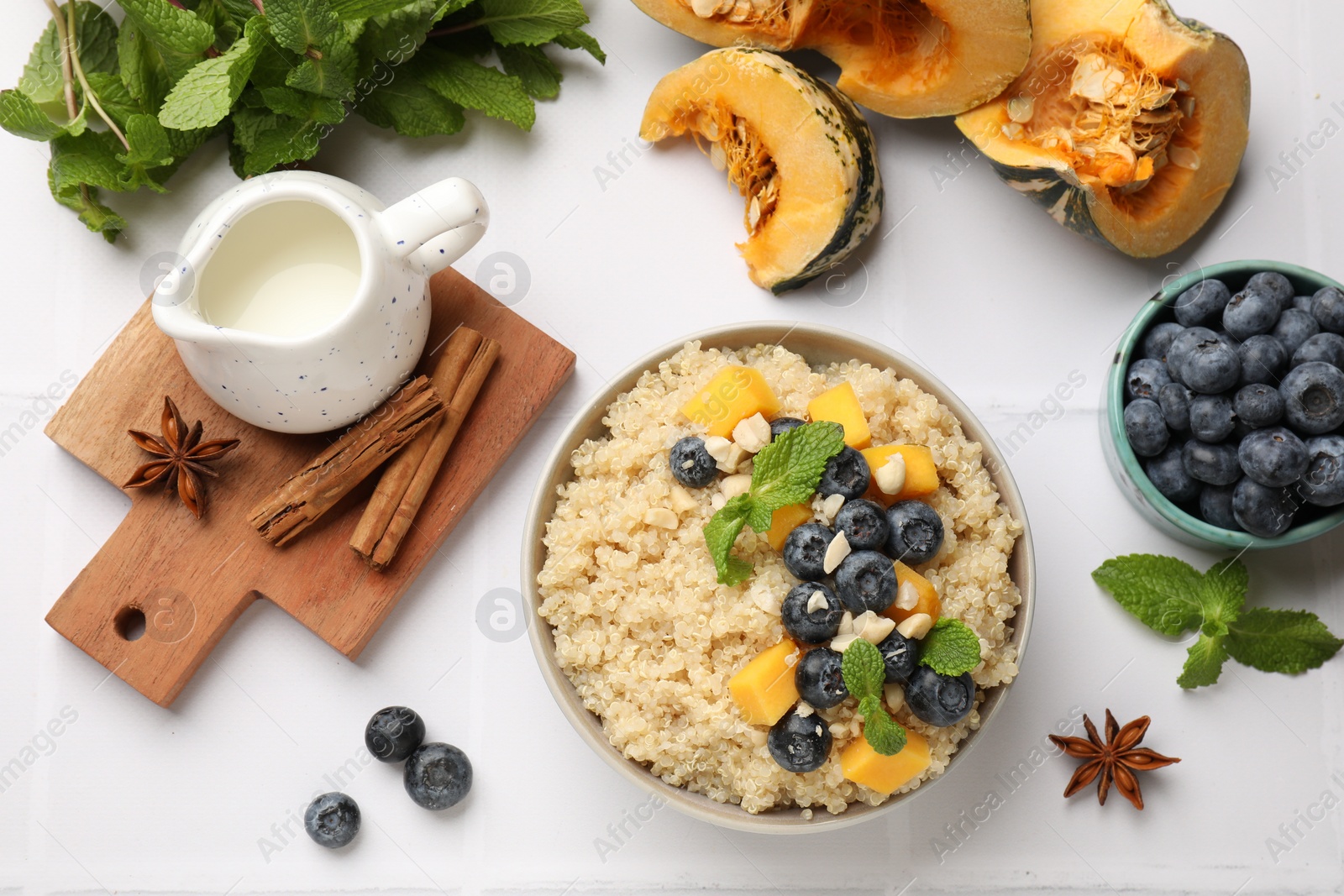 Photo of Flat lay composition with bowl of tasty quinoa porridge, blueberries and pumpkin on white tiled table