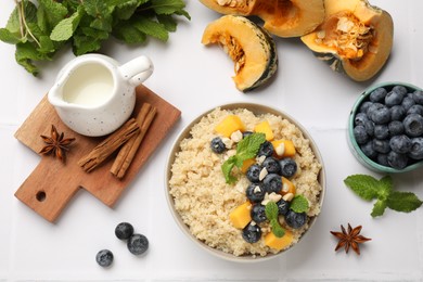 Photo of Flat lay composition with bowl of tasty quinoa porridge, blueberries and pumpkin on white tiled table