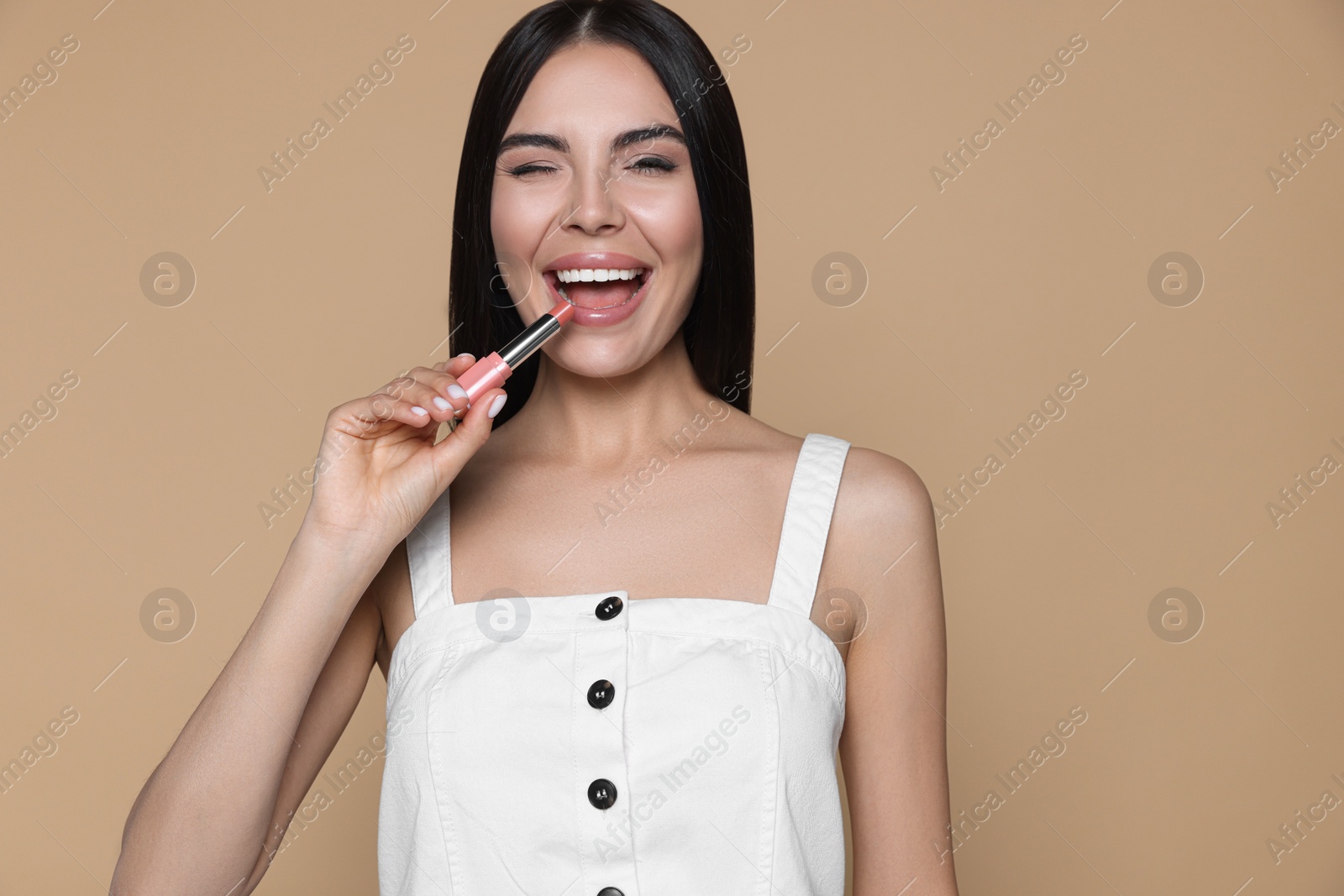 Photo of Young woman with beautiful makeup holding nude lipstick on beige background