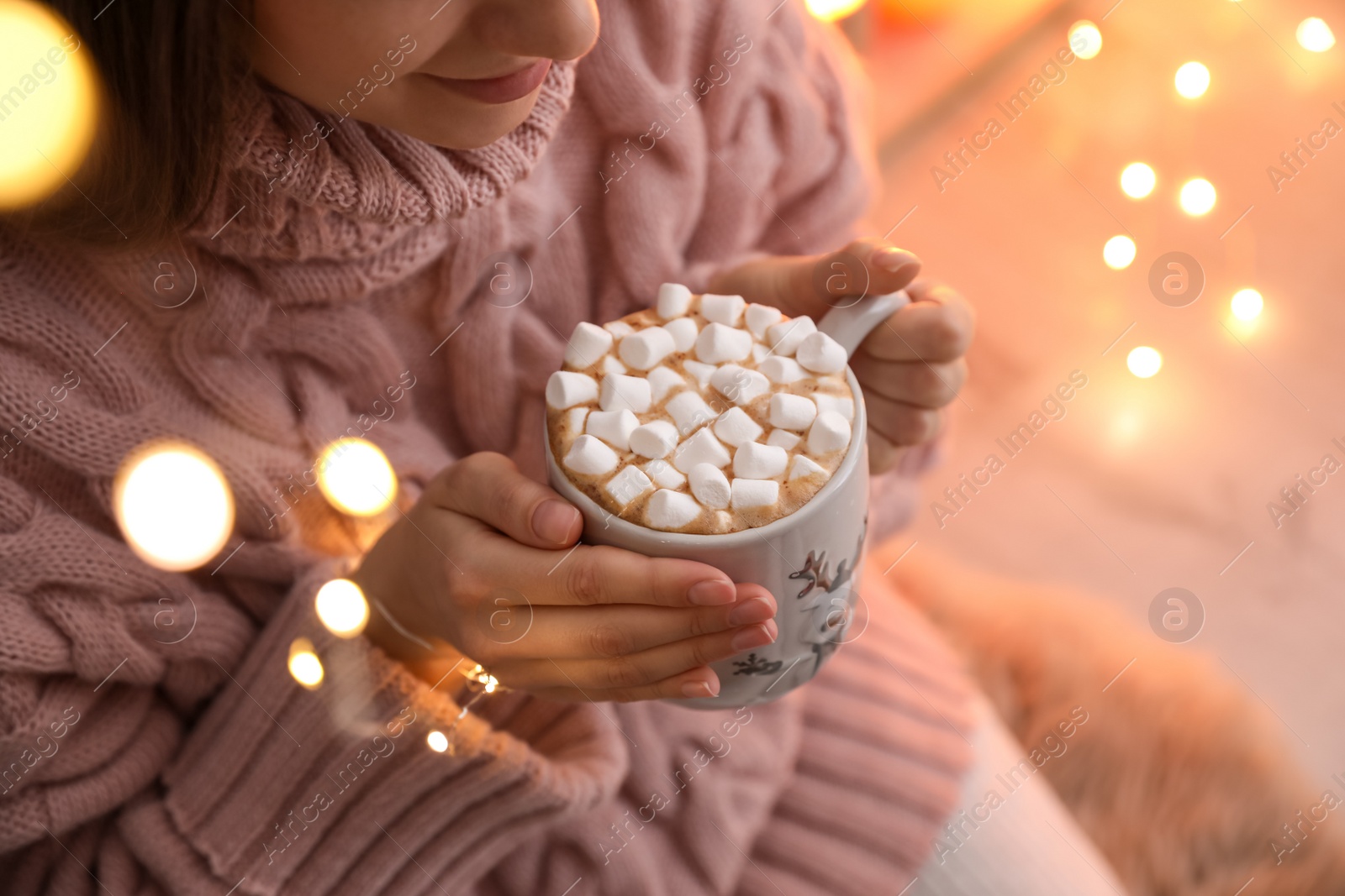 Photo of Woman holding cup of hot drink with marshmallows indoors, closeup. Magic Christmas atmosphere