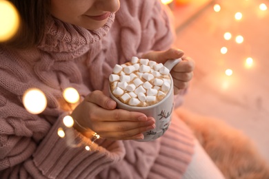 Photo of Woman holding cup of hot drink with marshmallows indoors, closeup. Magic Christmas atmosphere