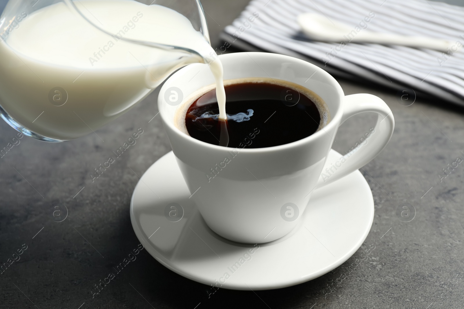 Photo of Pouring milk into cup of hot coffee on grey table