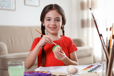 Photo of Little girl painting decorative egg at table indoors. Creative hobby