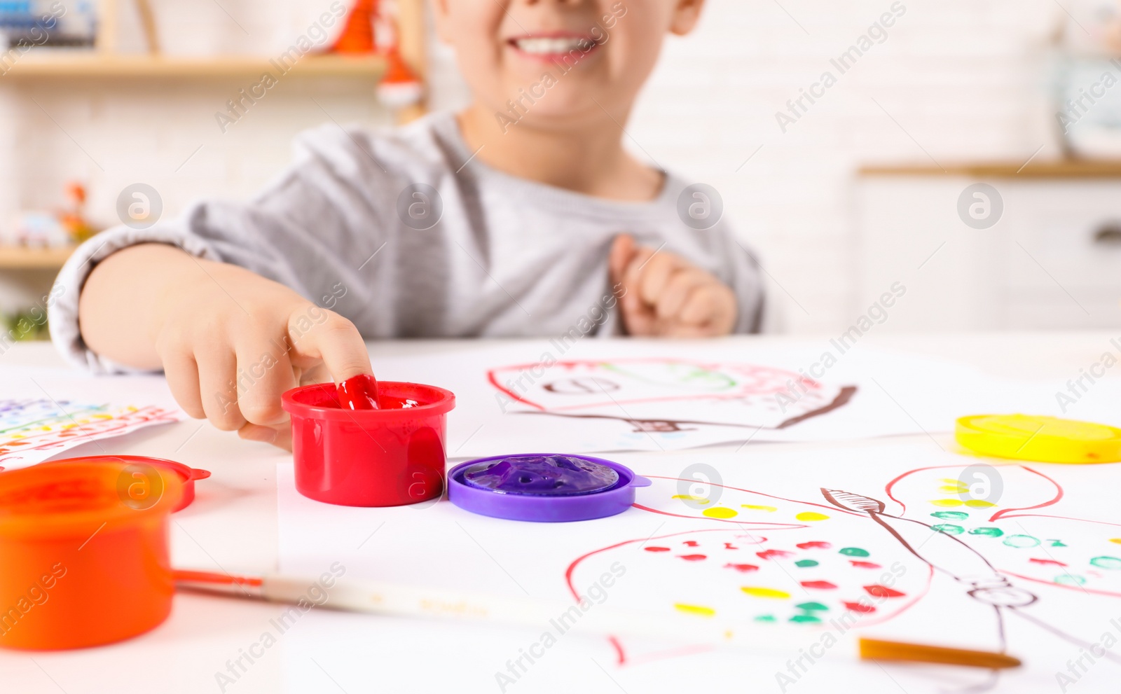 Photo of Little boy painting with finger at white table indoors, focus on hand