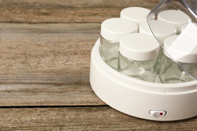 Modern yogurt maker with empty jars on wooden table, closeup. Space for text