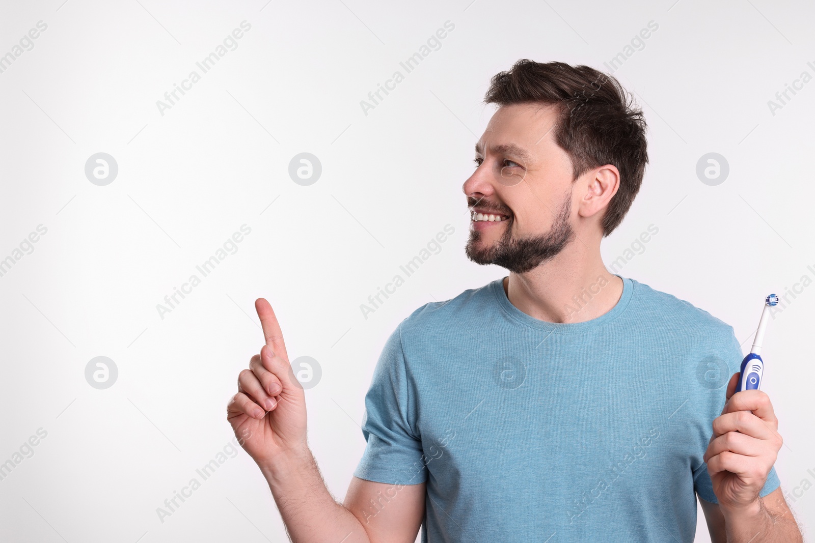 Photo of Happy man holding electric toothbrush on white background. Space for text