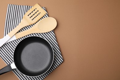 Different kitchen utensils, napkin and frying pan on light brown background, flat lay. Space for text