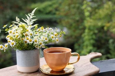 Photo of Cup of delicious chamomile tea and fresh flowers outdoors. Space for text