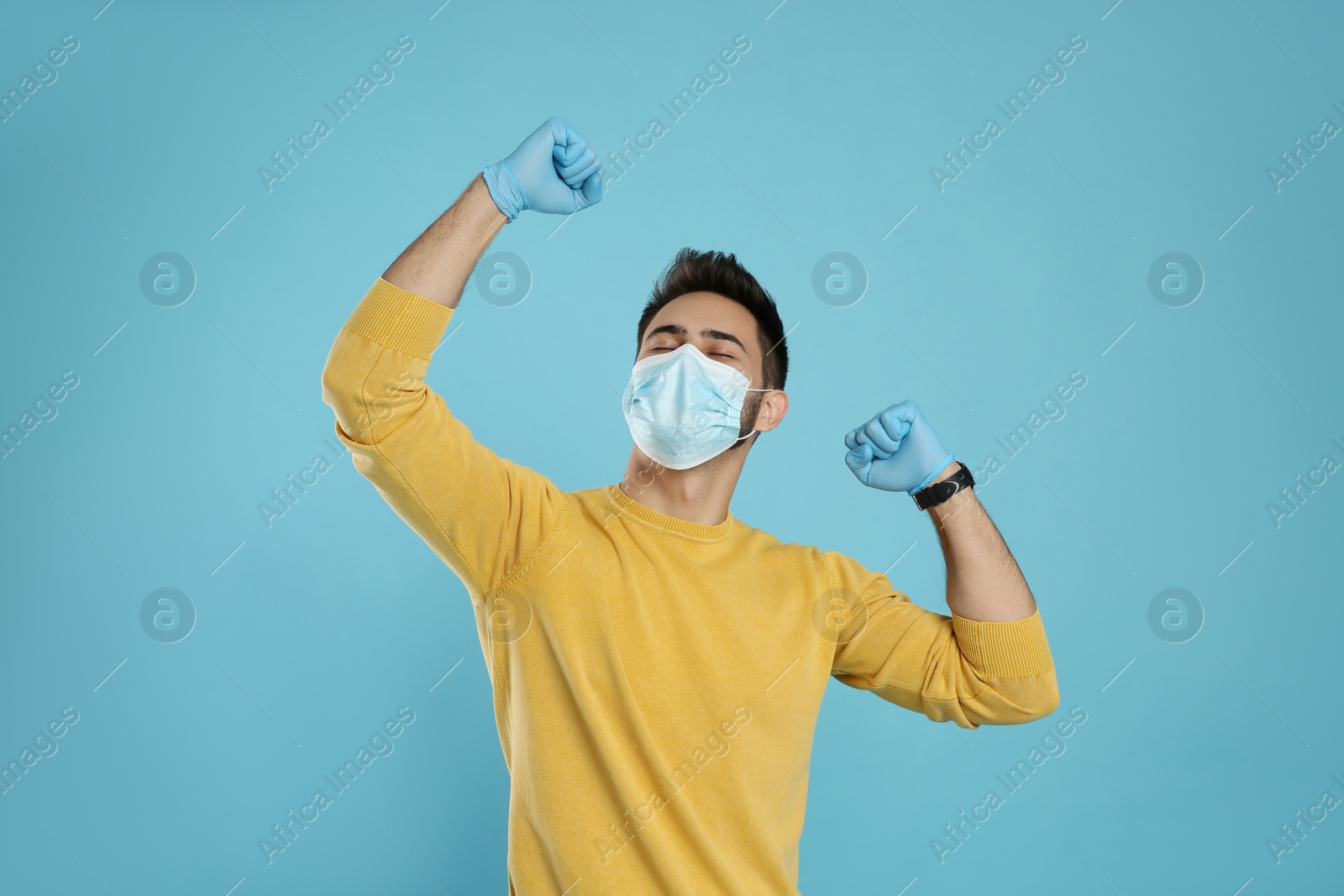 Photo of Emotional man with protective mask and gloves on light blue background. Strong immunity concept