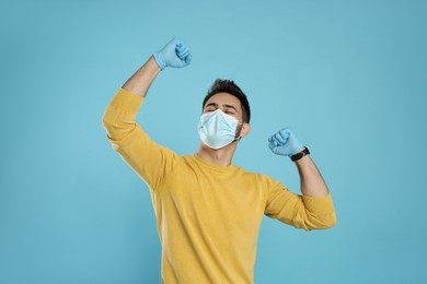 Emotional man with protective mask and gloves on light blue background. Strong immunity concept