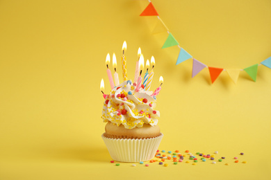 Photo of Birthday cupcake with candles on yellow background