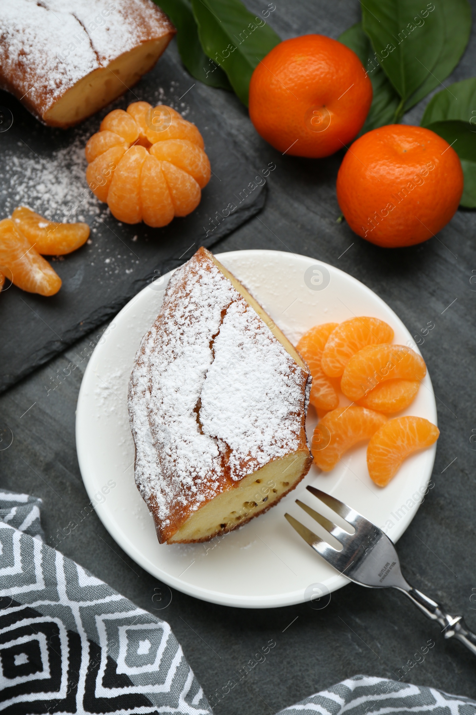 Photo of Piece of delicious homemade yogurt cake with powdered sugar and tangerines on gray table, flat lay