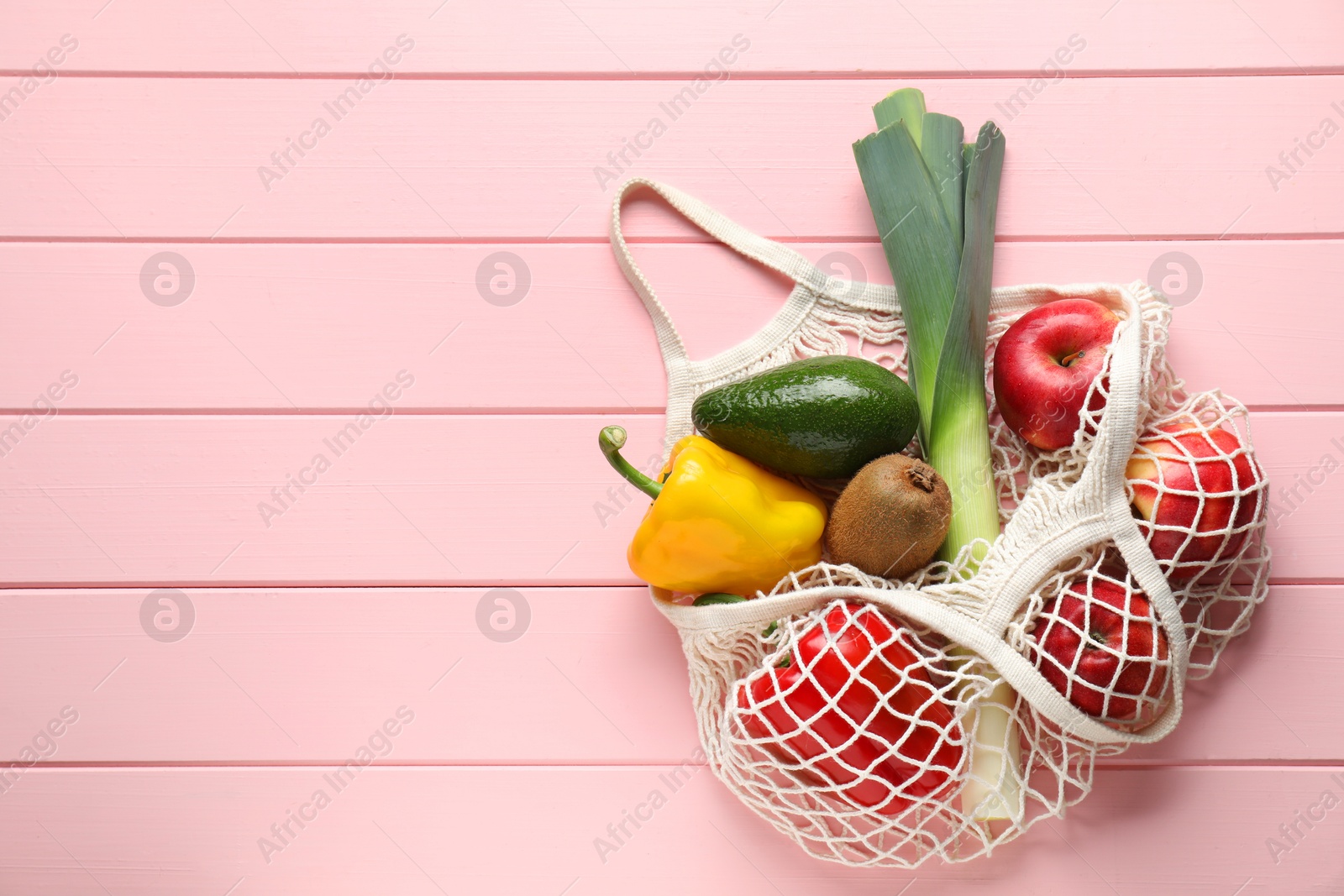 Photo of String bag with different vegetables and fruits on pink wooden table, top view. Space for text