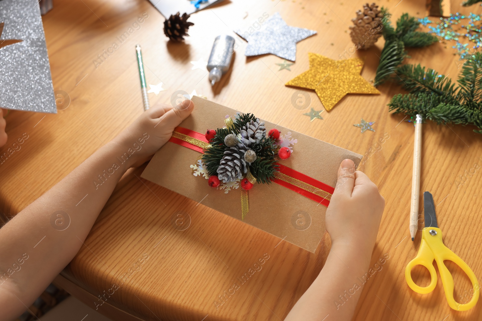 Photo of Little child with beautiful Christmas greeting card at wooden table, closeup