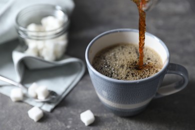 Pouring hot coffee into cup on grey table, closeup