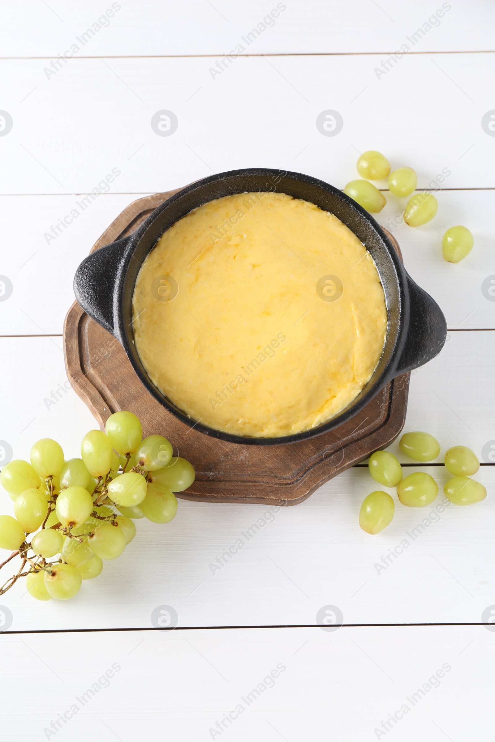 Photo of Fondue with tasty melted cheese and grapes on white wooden table, flat lay