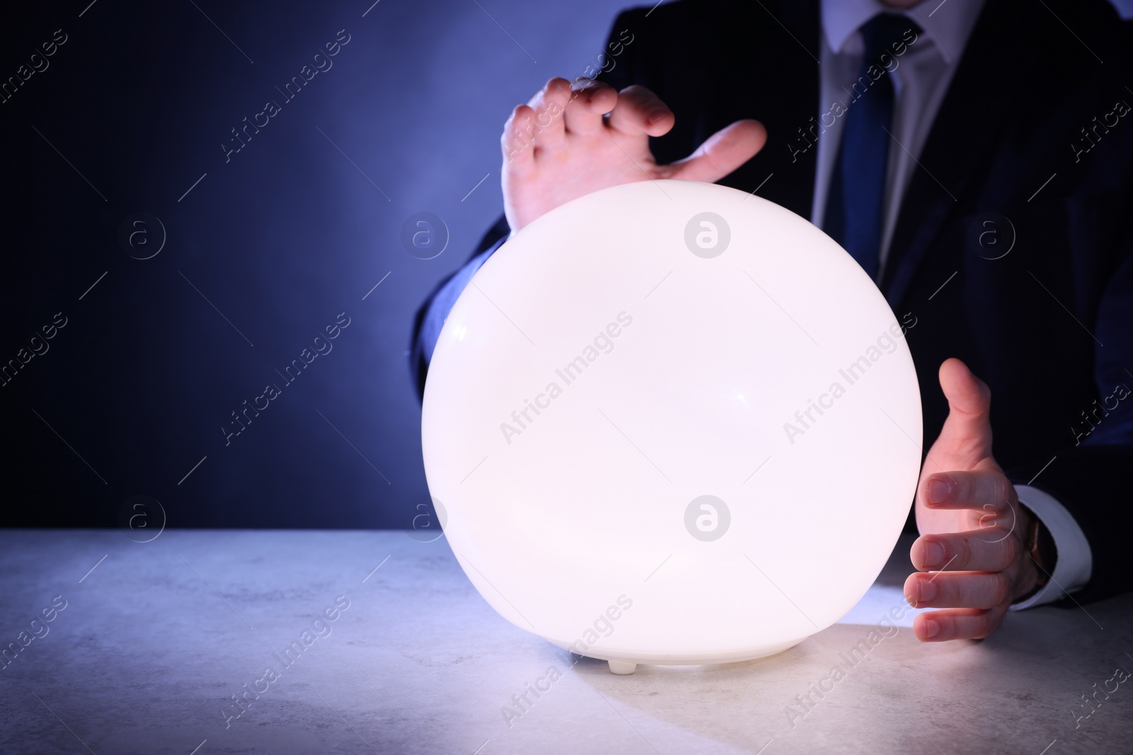 Photo of Businessman using glowing crystal ball to predict future at table, closeup. Fortune telling