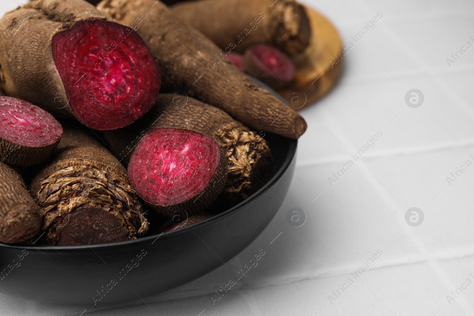 Photo of Whole and cut red beets in bowl on white table, closeup