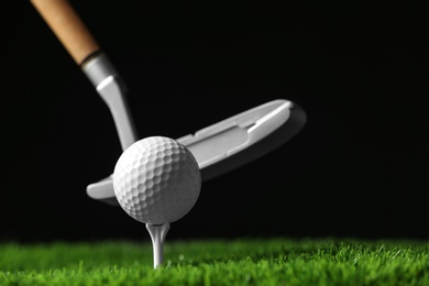 Photo of Hitting golf ball with club on artificial grass against black background, space for text