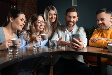 Photo of Handsome man showing something funny in smartphone to his friends in cafe