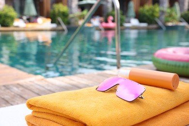 Photo of Beach towels, sunglasses and sunscreen on sun lounger near outdoor swimming pool at luxury resort. Space for text