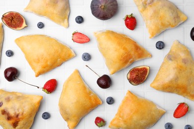 Photo of Delicious samosas, berries and fig on white tiled table, flat lay