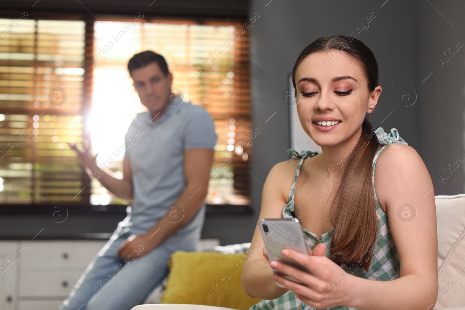 Photo of Woman preferring smartphone over spending time with her boyfriend at home. Jealousy in relationship