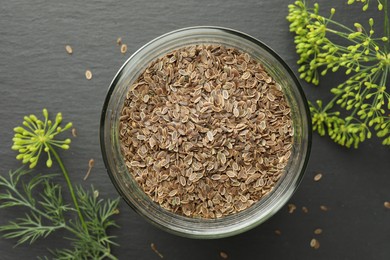 Photo of Dry seeds and fresh dill on black table, flat lay