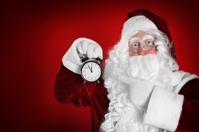 Photo of Santa Claus holding alarm clock on red background. Christmas countdown