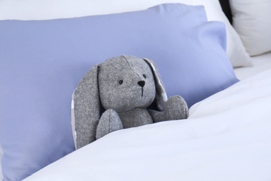 Photo of Cute toy rabbit lying in bed indoors