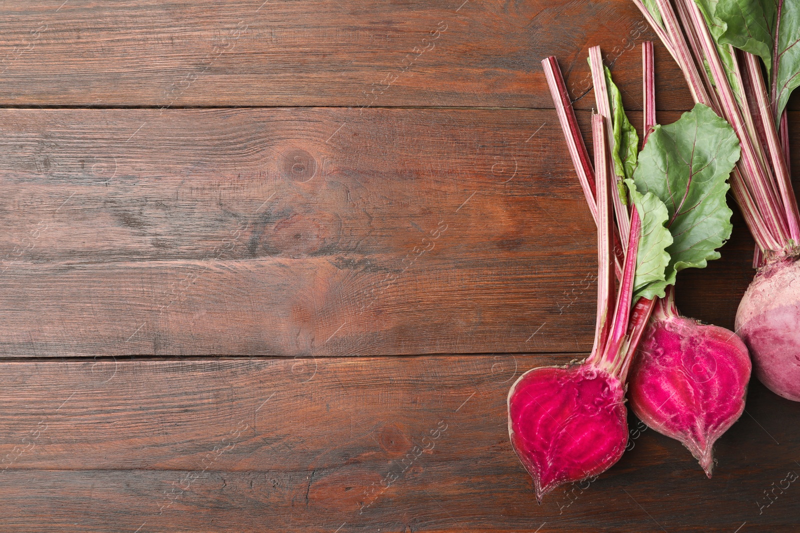 Photo of Cut and whole raw beets on wooden table, flat lay. Space for text