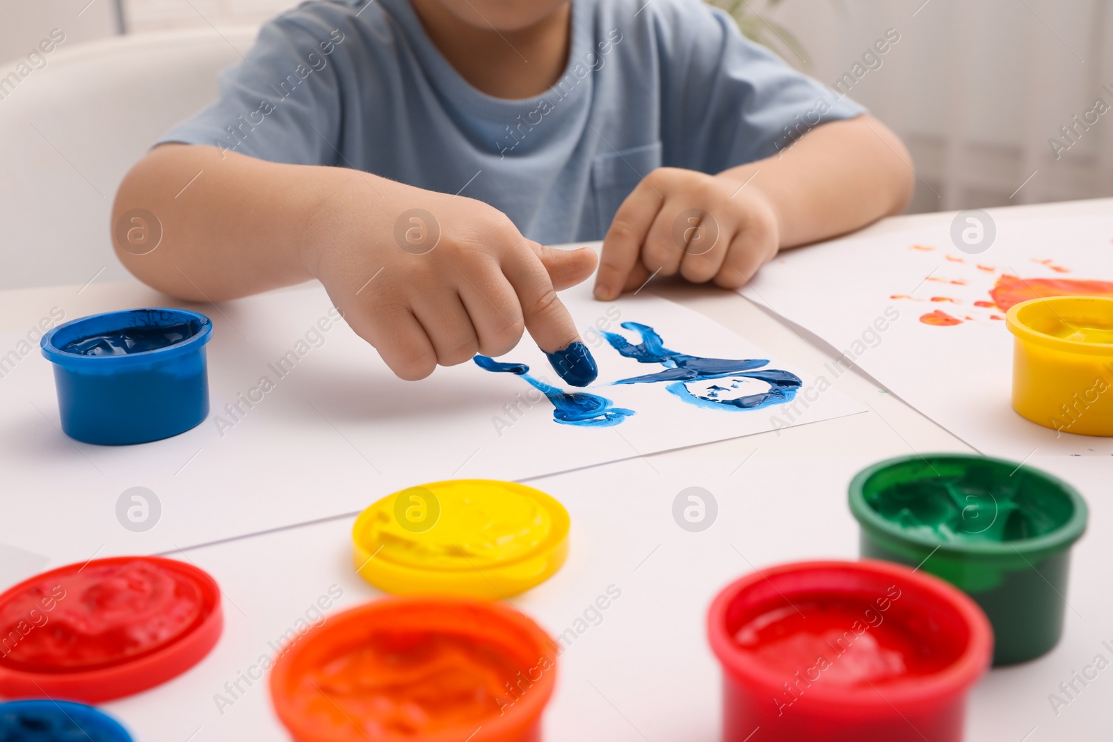 Photo of Little child painting with finger at white table indoors, closeup