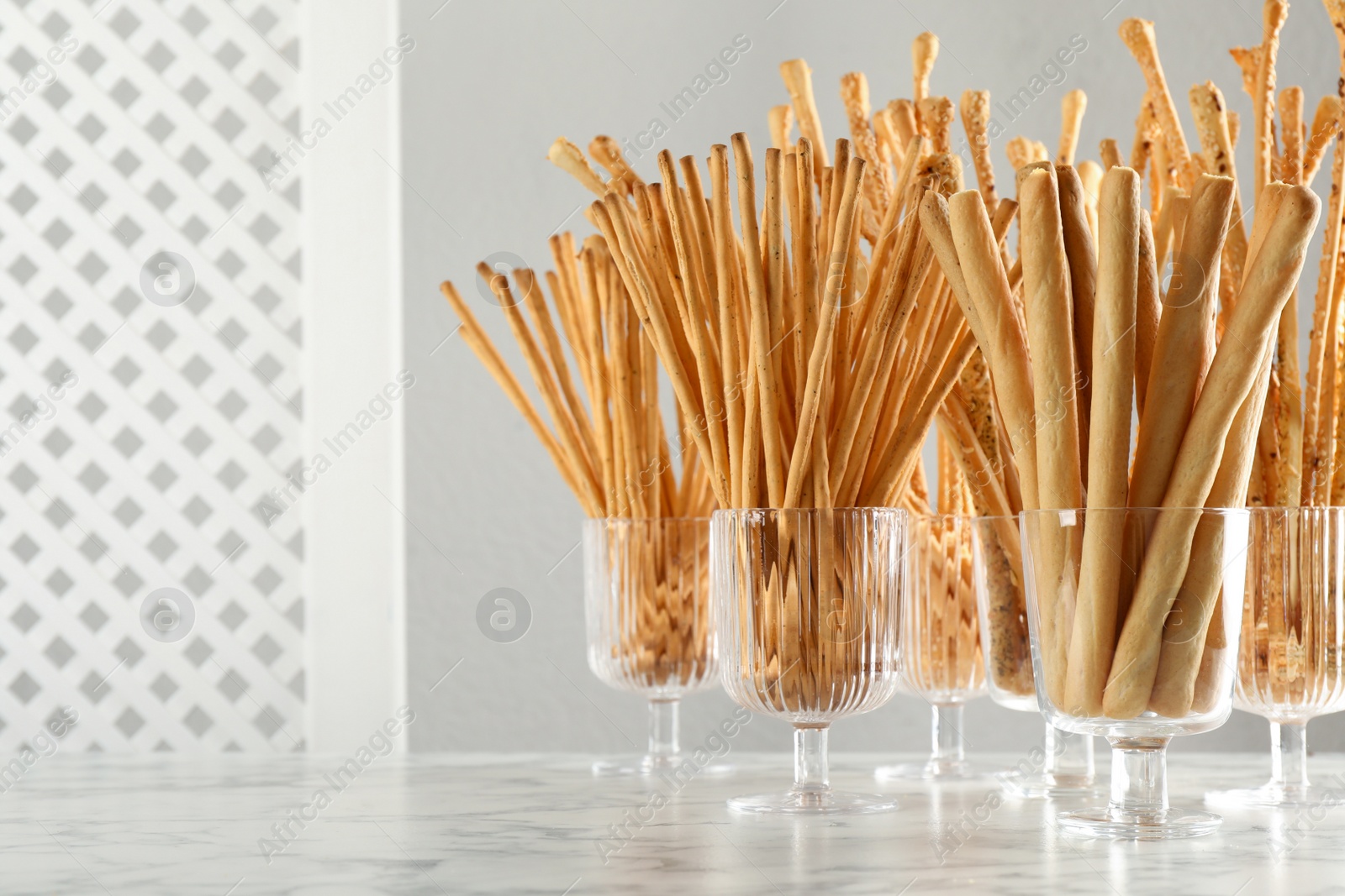 Photo of Delicious grissini sticks served in glasses on white marble table. Space for text