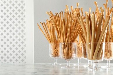 Delicious grissini sticks served in glasses on white marble table. Space for text