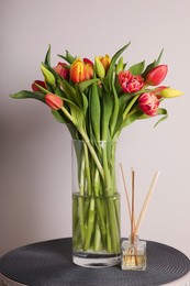 Beautiful bouquet of colorful tulips in glass vase on table against pink background