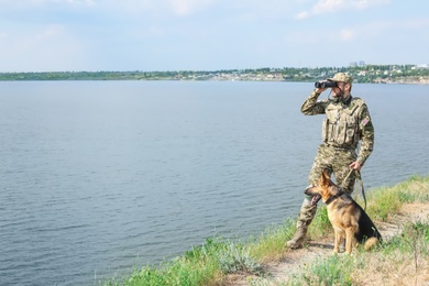 Photo of Man in military uniform with German shepherd dog outdoors