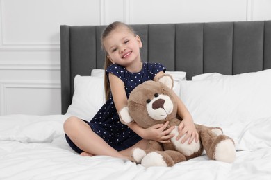 Photo of Cute little girl playing with teddy bear on bed