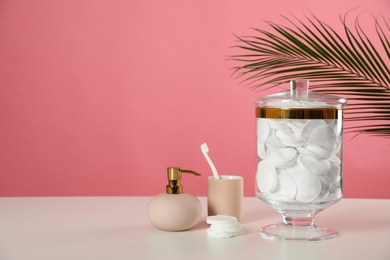 Jar with cotton pads on white table against pink background. Space for text