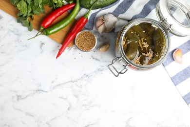 Flat lay composition with jar of pickled cucumbers on white marble table, space for text