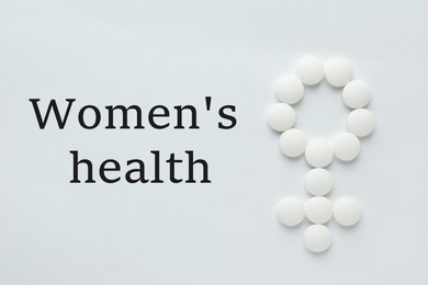 Photo of Words Women's Health and female symbol made of pills on white background, flat lay